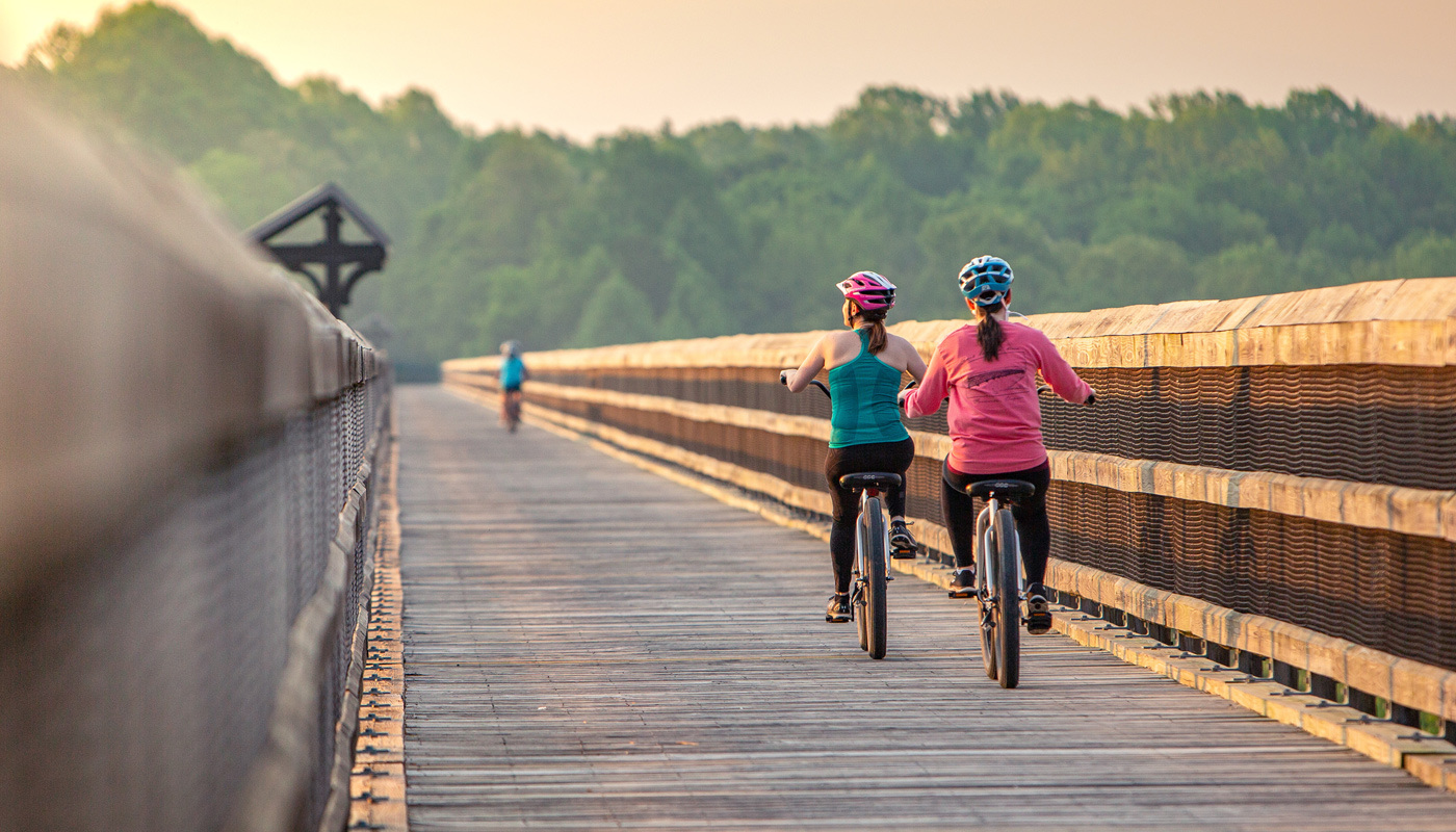 Two girls wearing helmets riding bikes across a bridge trail