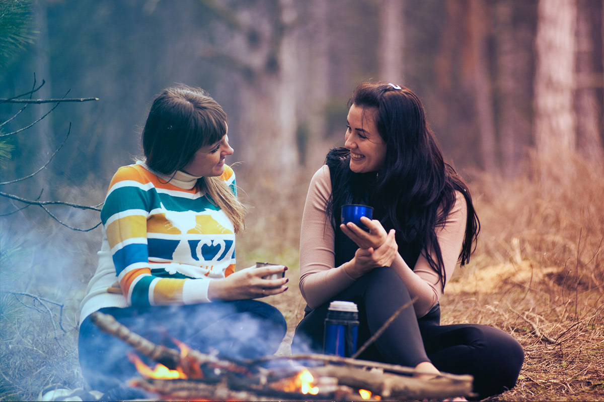 Two girls sitting outdoors by a small fire